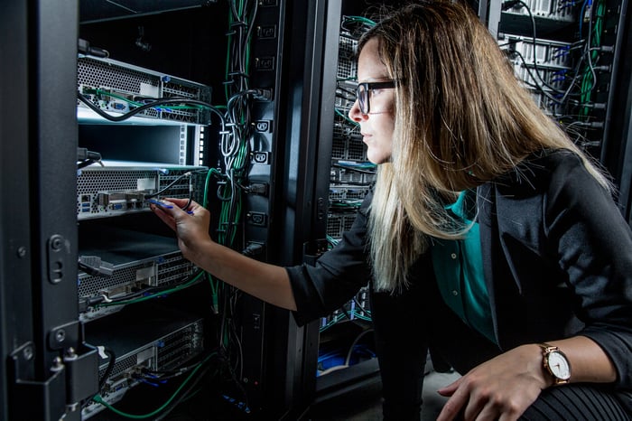 An engineer checking switches and wires on the back of a data center server tower. 