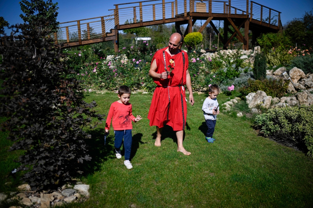 Tsvetomir Tsonev, 47, dressed in a red toga, walks with his sons, named with Tracian names in his garden of roses and medicinal plants opened to the public in the village of Neofit Rilski, north-east Bulgaria October 10, 2024. — AFP pic