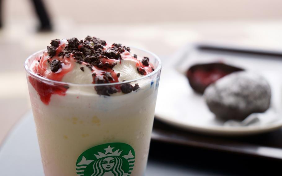 A colorful drink with a cup with a Starbucks logo sits in the foreground. A brown, sugar-dusted pastry with red filling exposed sits out of focus in the background.