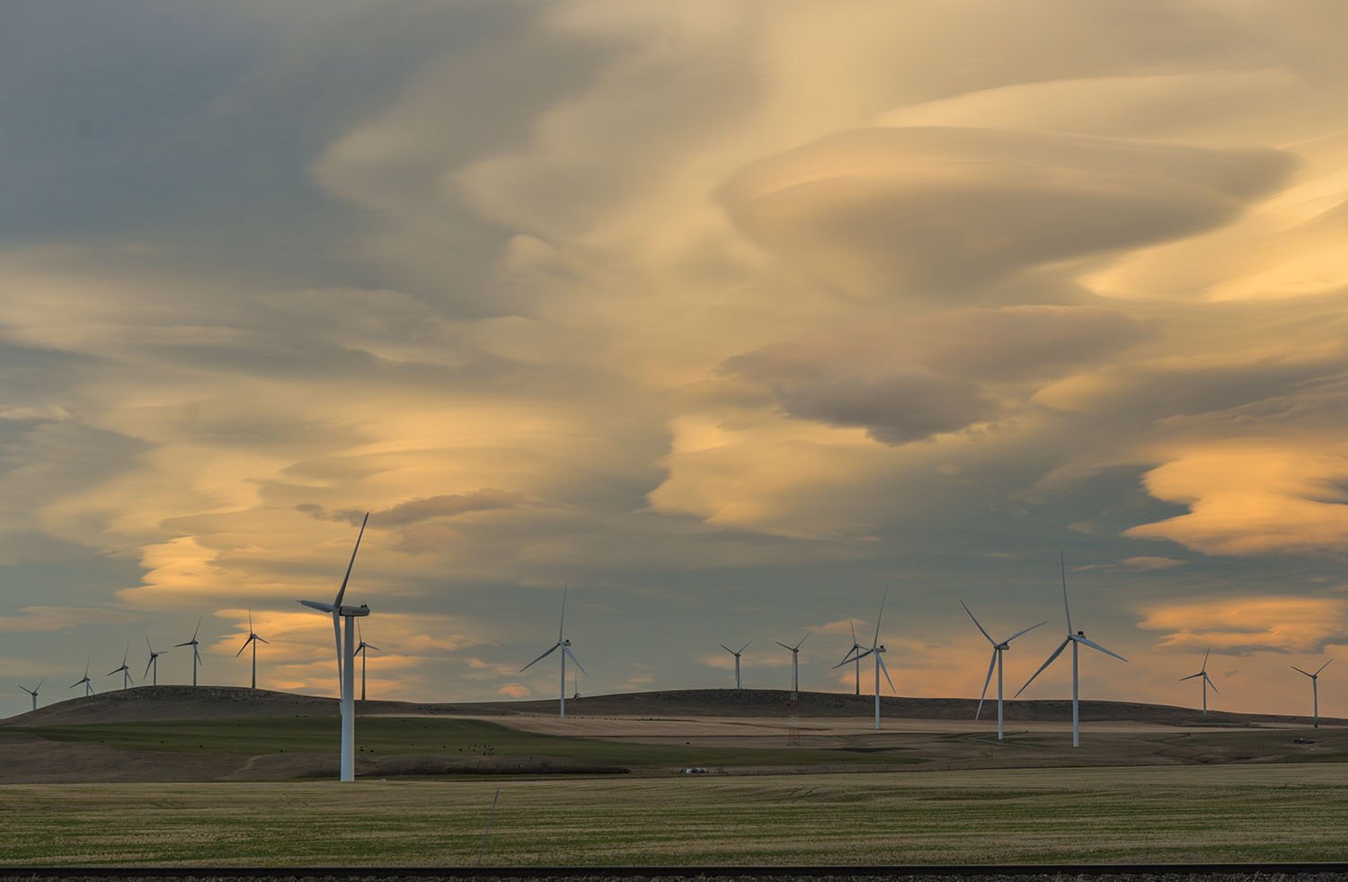 Large wind turbines stand in a field against a sky with swirling clouds.