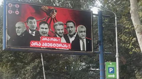 "No to war, no to agents" is the message beneath pictures of six opposition leaders, who are each held by a leash