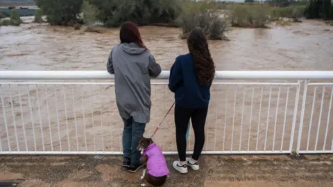 Getty Images Two women and a dog look out over the flooded Magre River, in Valencia region - 30 October 2024