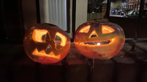 BBC Two carved pumpkins sit on a wall. It's night time and the candles inside illuminate them.