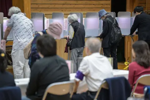 Getty Images Officials look on as people vote during the general election at a polling station set up at a local school in Tokyo on October 27, 2024