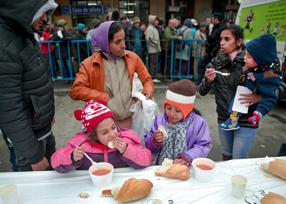 In this Wednesday, Dec. 16, 2015 file photo, homeless children eat as others wait in line for their turn outside the main railway station in Bucharest, Romania. (AP)