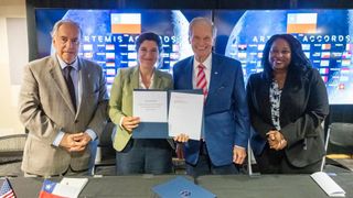 two men and two women stand behind a table, with two of them holding up documents for the camera