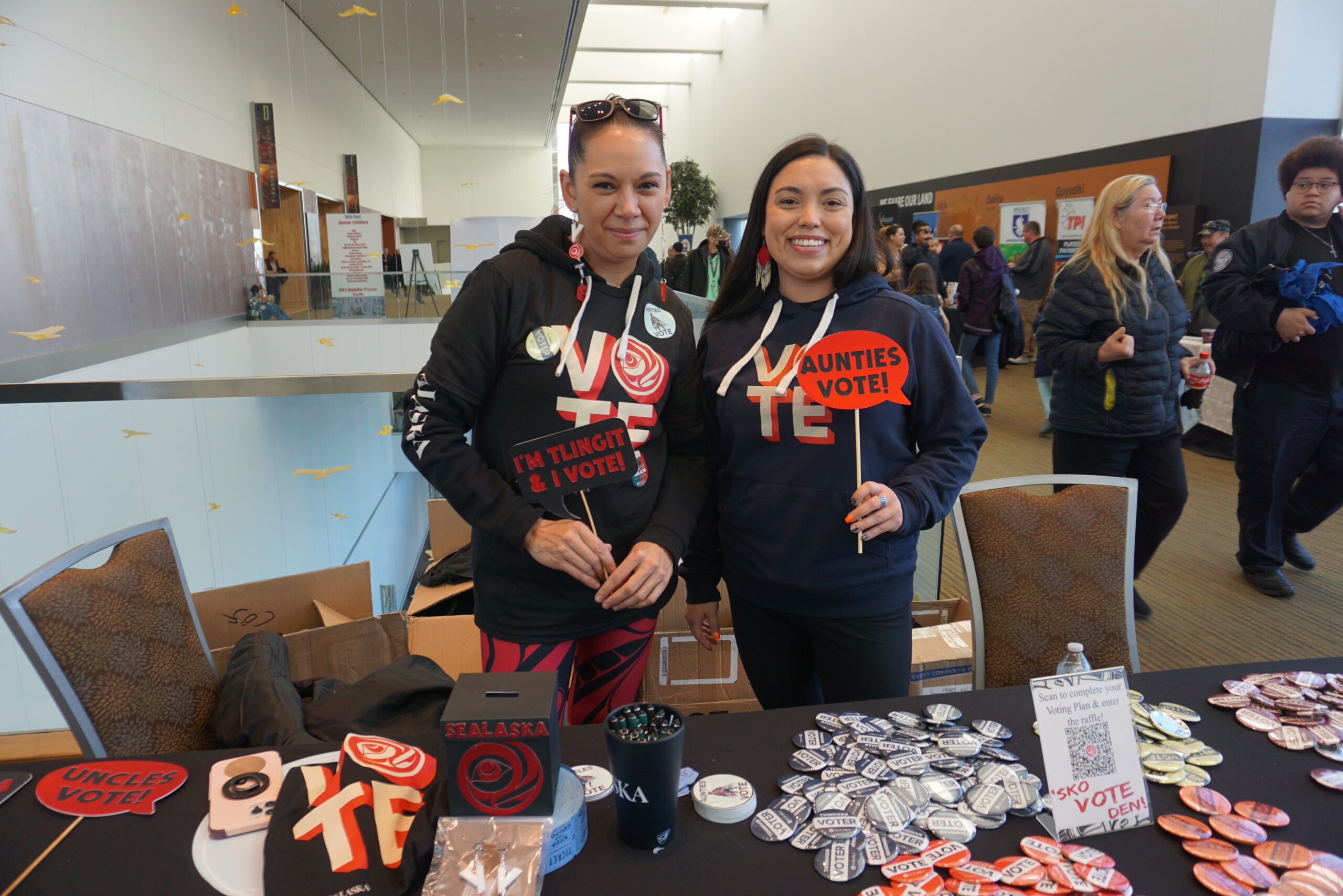 Sarah Antioquia and Vanessa Allen, mannng a Sealaska booth at the Alaska Convention of Natives convention on Oct. 18, 2024, display buttons and signs encouraging Native voting. (Photo by Yereth Rosen/Alaska Beacon)