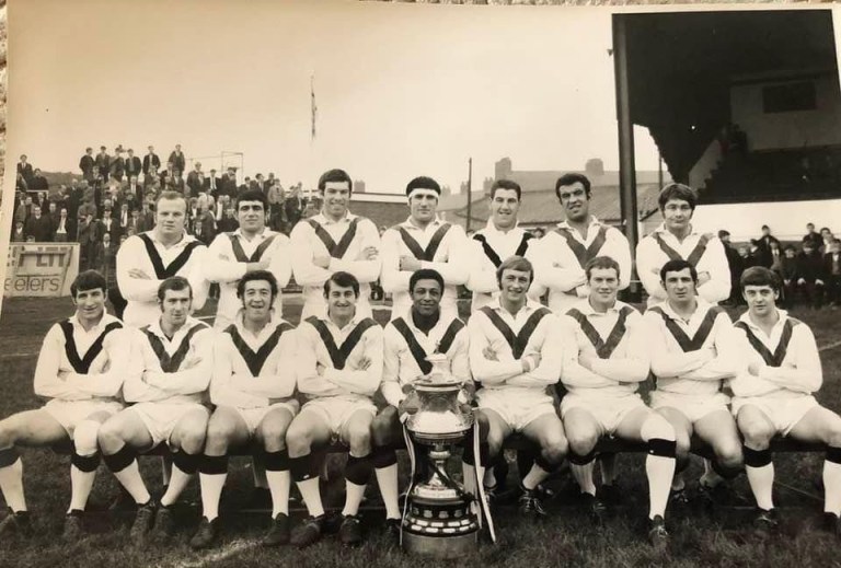 Team photo of a rugby team with a trophy in front of them – Clive Sullivan is seated in the middle of the front row