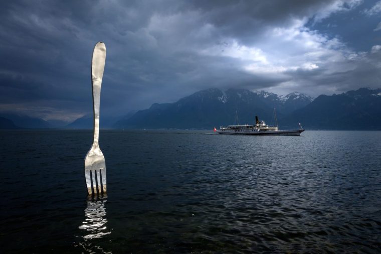 A picture taken on May 21, 2019 in Vevey shows the paddle steamer 'Italie' of the Compagnie Generale de Navigation sur le lac Leman, commonly abbreviated to CGN, sailing on Lake Geneva past a giant fork sculpture designed by Switzerland's artist Jean-Pierre Zaugg. (Photo by Fabrice COFFRINI / AFP) / RESTRICTED TO EDITORIAL USE - MANDATORY MENTION OF THE ARTIST UPON PUBLICATION - TO ILLUSTRATE THE EVENT AS SPECIFIED IN THE CAPTION (Photo credit should read FABRICE COFFRINI/AFP via Getty Images)