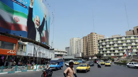 EPA Cars and people on a street in Tehran with a large billboard showing an image of former Hamas leader Ismail Haniyeh (file photo)