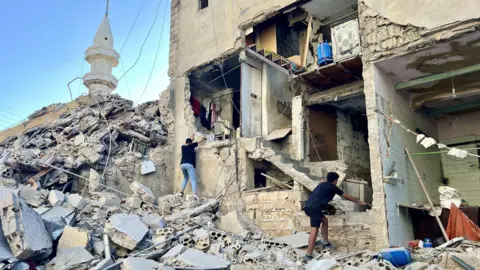 EPA People inspect a damaged building after an Israeli strike on the city of Tyre, Lebanon (23 October 2024)