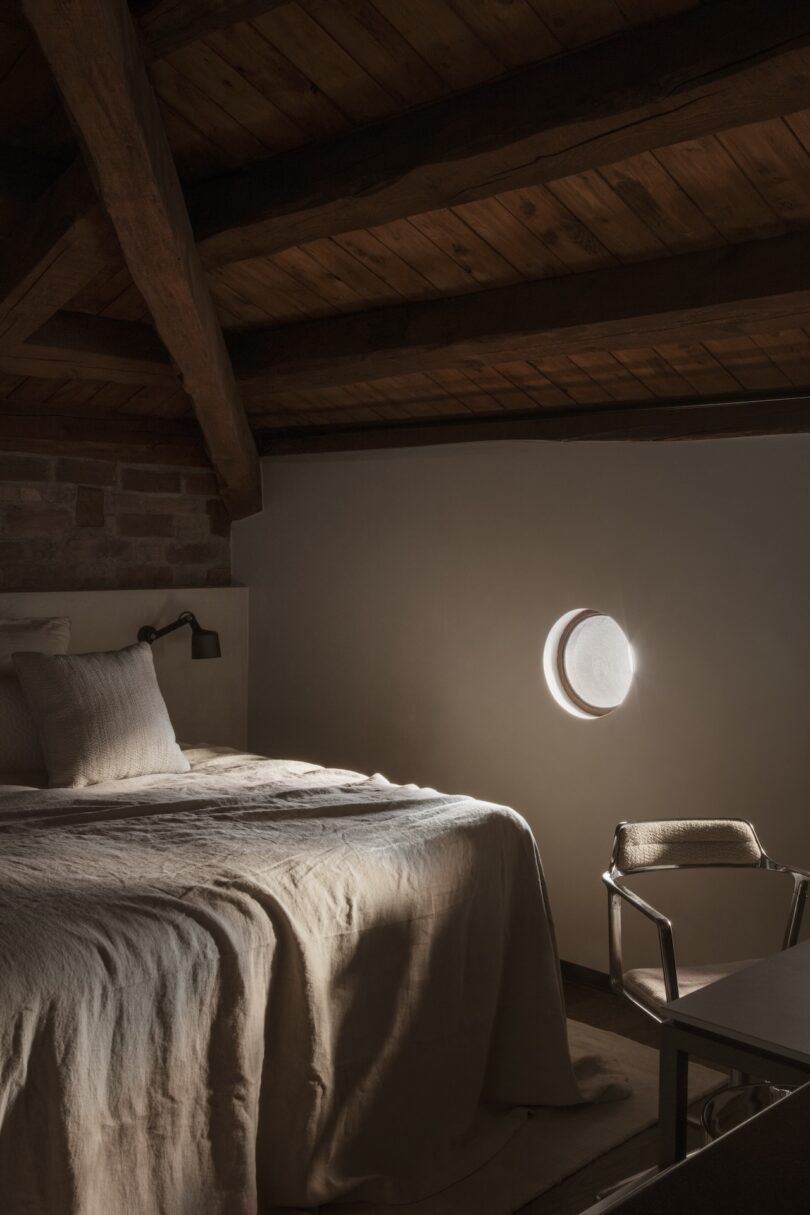 A tranquil bedroom with wooden beams, a port window, and a cozy linen bedspread