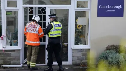 Andrew Matthews/PA White glazed entrance with backs of police officer and fire fighter standing in the doorway