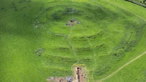 Other The site of Tlachtga in a drone image, showing a large green area which dips down showing small paths and patches of mudded areas where bonfires would have been lit. 