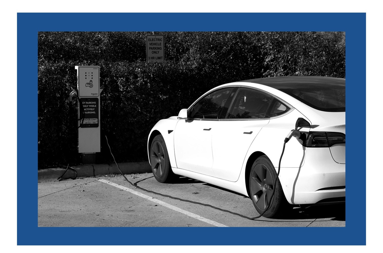 A black and white photo of an electric car plugged into a charger. The photo has a blue border around it.