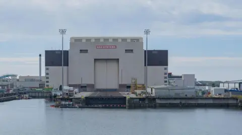 Getty Images A side view of a large hanger that makes up part of the BAE Systems nuclear submarine shipyard in Barrow-in-Furness. The hanger backs onto a small port of water.