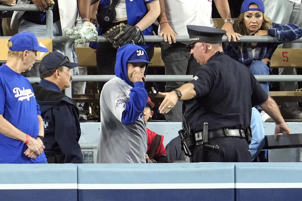 A law enforcement officer talks with a fan who reached over the outfield wall to catch a fly ball by New York Yankees' Gleyber Torres during the ninth inning in Game 1 of the baseball World Series, Friday, Oct. 25, 2024, in Los Angeles. (AP Photo/Godofredo A. Vásquez)