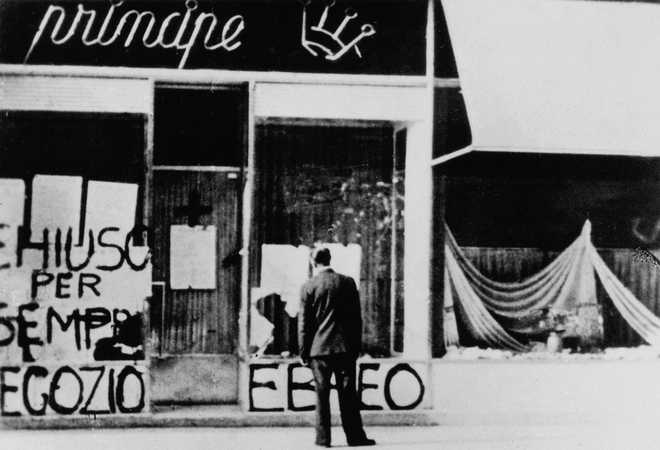 An Italian man watching the anti-Semitic graffiti and broken windows of a Jewish store picked on by Fascists. Trieste, 1942 (Photo by Mondadori via Getty Images)