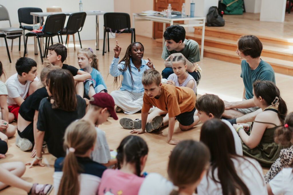 Children sit in a circle as if playing the game duck, duck, goose.