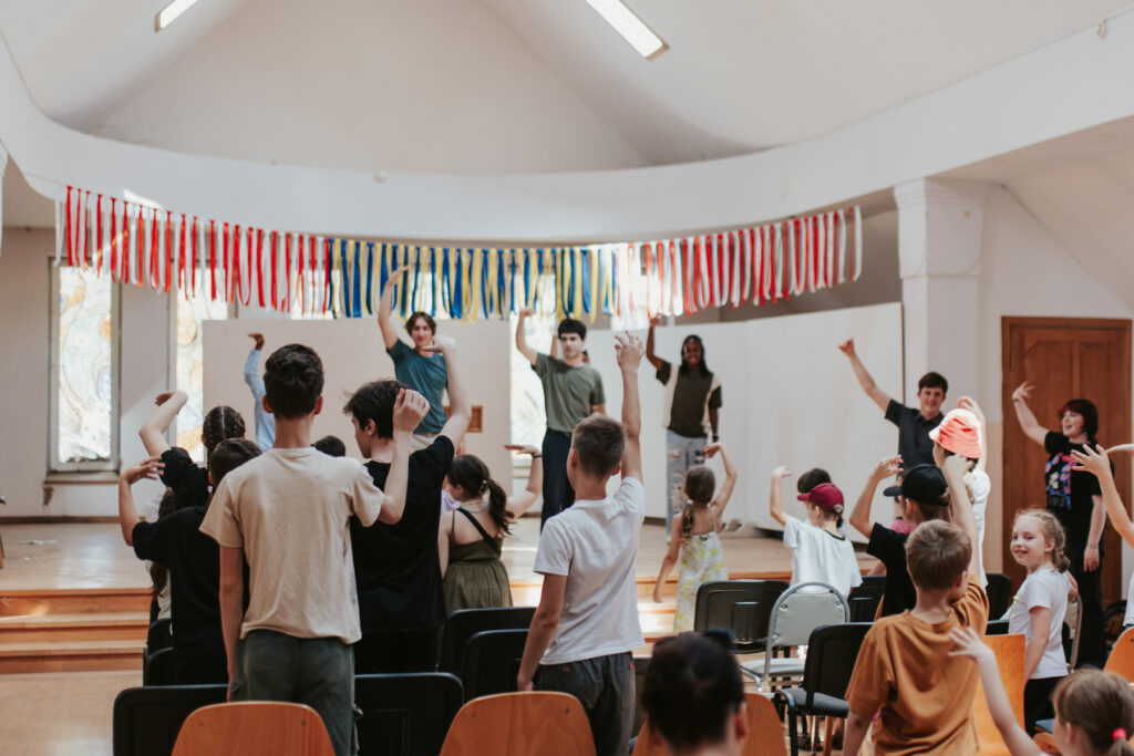 College students stand on an indoor stage leading children in an activity.