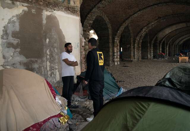 An IRC officer speaks with an asylum seeker in Italy. They stand nearby a series of tents.