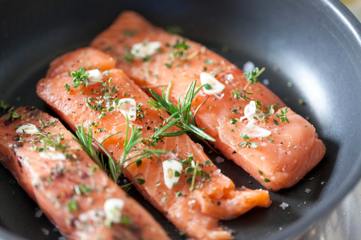 Salmon topped with garlic and herbs in a black frying pan.